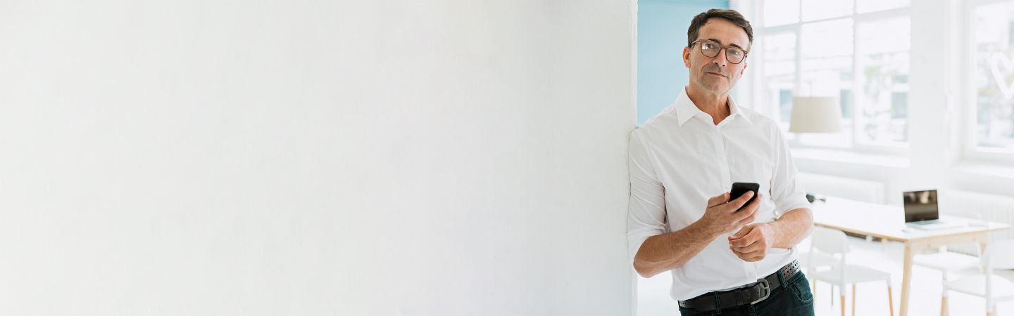 Section Stage Man Business A man in a white shirt leans against a wall, holds his smartphone in his hand and looks seriously into the camera